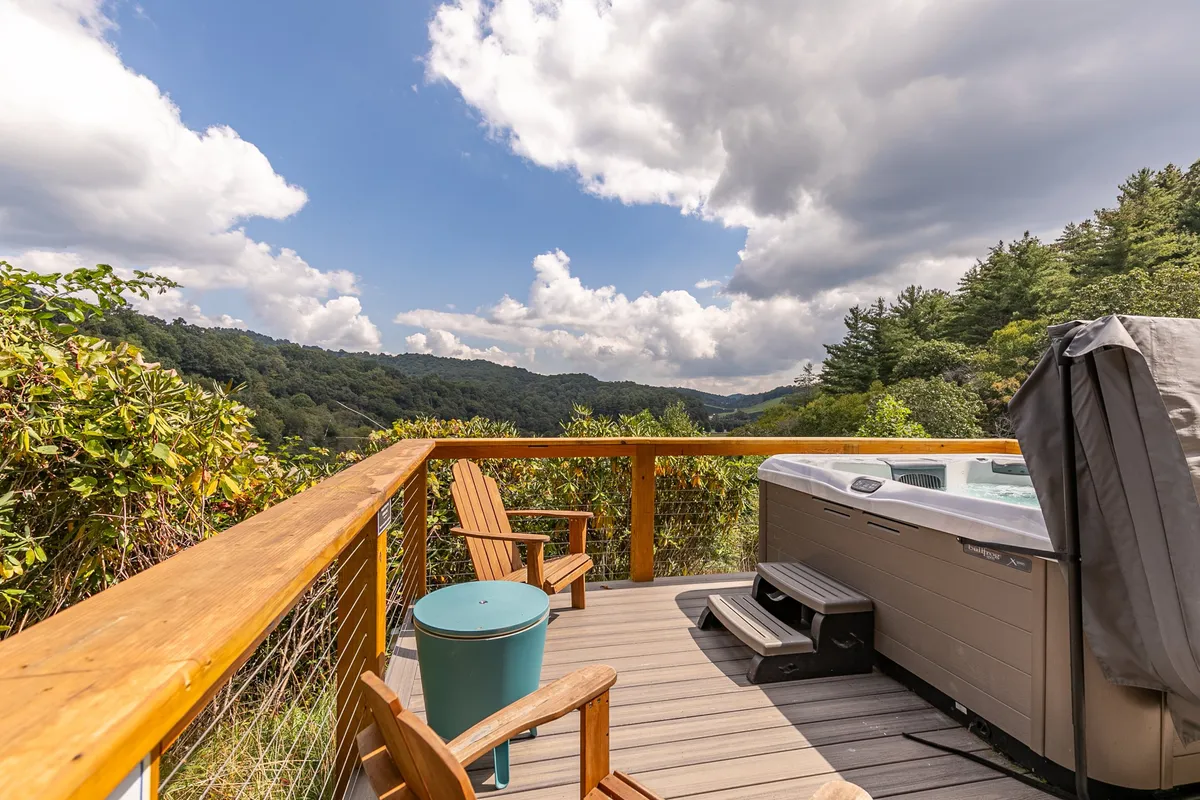 A relaxing wooden deck features a steaming hot tub, Adirondack chairs, and a breathtaking mountain view. The peaceful setting suggests the ideal place to unwind after a day of adventure, with opportunities for stargazing or sharing stories with friends.