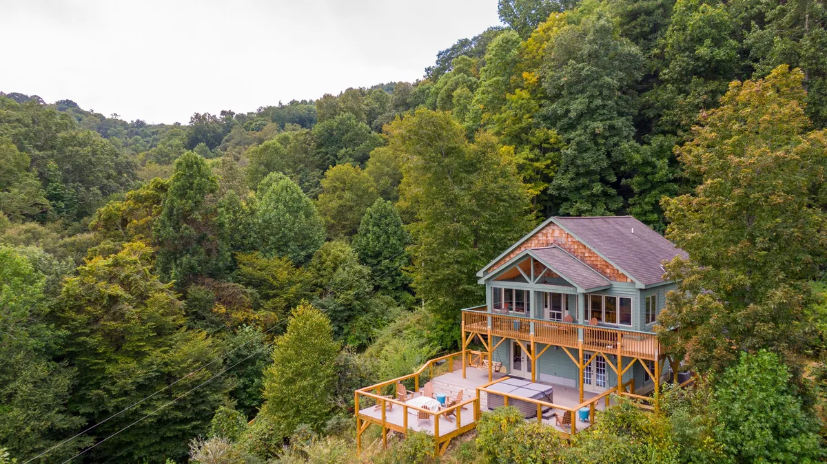 A wide-angle view of the house’s exterior, showcasing spacious multi-level decks surrounded by towering trees. The deck is furnished, inviting groups to relax, dine, or watch nature, while the home’s architecture blends into the serene landscape.