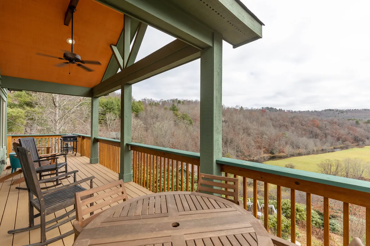 A spacious wooden deck set with classic rocking chairs and a circular wooden table, overlooking a serene valley. The deck is bordered by secure railings, and the views of the surrounding nature provide a relaxing backdrop perfect for both pets and owners. The setup is inviting for lounging and socializing, with plenty of space for pets to rest close by.