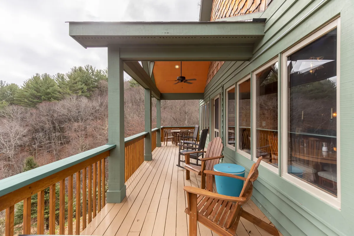 A wooden deck with rocking chairs and a blue accent table is nestled among tall trees, offering a tranquil outdoor seating area perfect for breaks or quiet reflection.