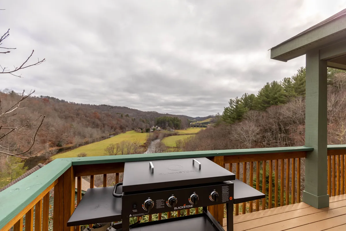 A grill sits on the deck with a stunning scenic view in the background, suggesting opportunities for outdoor cooking and dining while surrounded by nature's changing beauty.