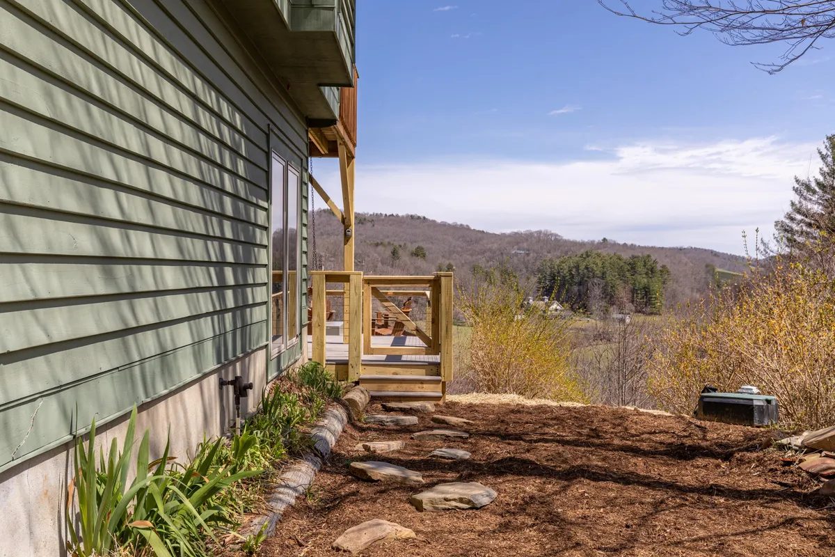 A wooden deck leads to a natural pathway surrounded by lush greenery. The deck provides a clear connection to the outdoor environment, making it an ideal starting point for scenic walks or playful exploration with pets. The surrounding garden and trees enhance the sense of nature immersion.