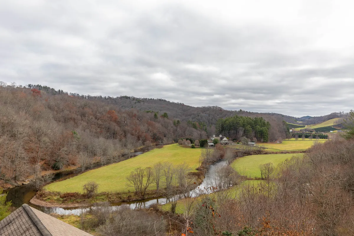 A sweeping view of a gently winding river flanked by lush green fields and wooded hills, with a few houses in the distance. The tranquil landscape evokes a sense of seclusion and opportunity for exploration—ideal for nature walks and riverside adventures.