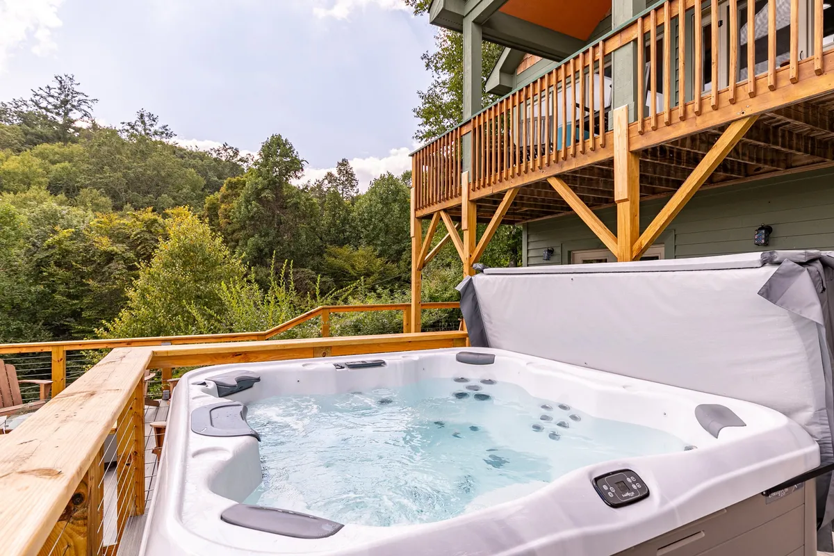 A dedicated hot tub area on a wooden deck, surrounded by mature trees, offers a tranquil spot for soaking while enjoying nature. The setting feels private and serene, perfect for unwinding after outdoor adventures.