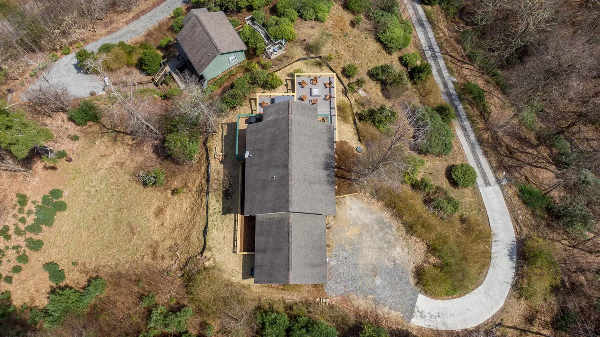 A wide shot of the property exterior, featuring a spacious house, patio area, and abundant greenery with a winding driveway. The expansive lawn and garden areas offer ample space for pets to play, while the tranquil setting invites guests to enjoy nature alongside their animals.