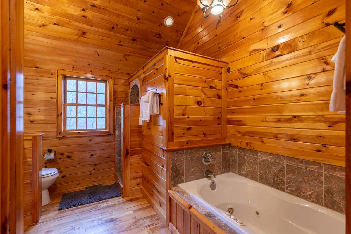 A spa-like bathroom with a beautiful wooden tub, separate shower area, wooden walls, and a window letting in natural light. The tranquil design and materials invite relaxation and self-care.