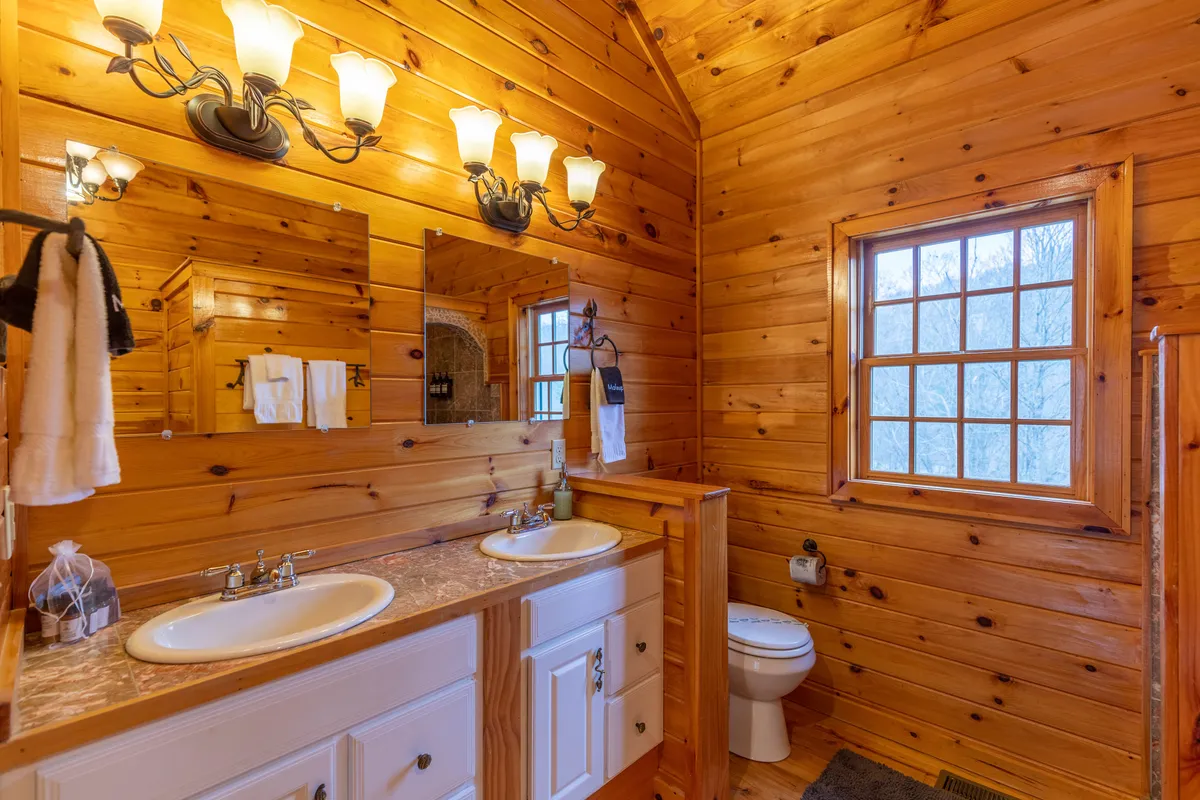 A double vanity bathroom with large mirrors, wooden walls, and a window streaming in natural light. The space feels airy and elegant, ideal for morning routines or unwinding at day’s end.