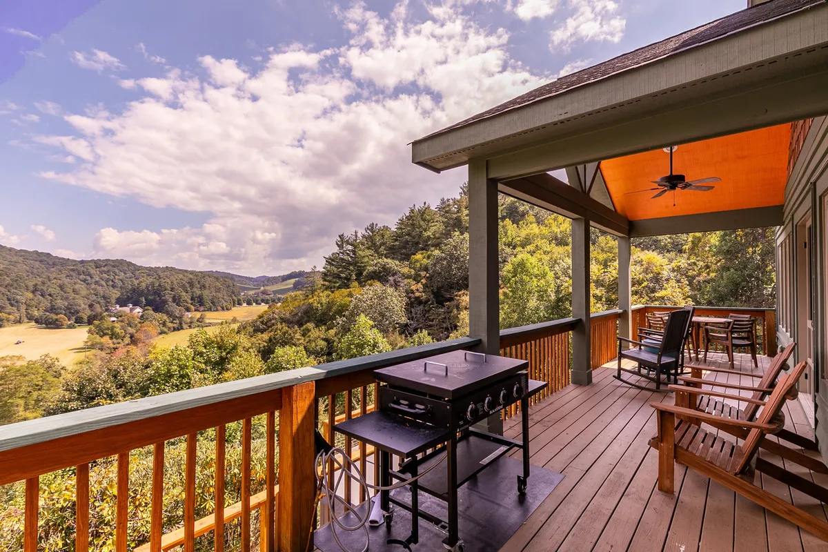 An inviting outdoor space with a grill, classic rocking chairs, and an expansive view of mountains and valleys. The setup encourages social gatherings, grilling fresh-caught fish, and enjoying nature’s grandeur.