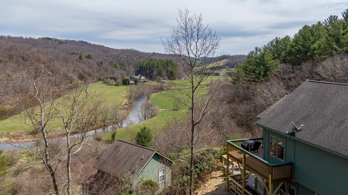 A lush, panoramic landscape with a meandering river, distant mountains, and a wooden deck in the foreground. The scene evokes adventure, with visible opportunities for fishing, hiking, and wildlife watching right outside the property.